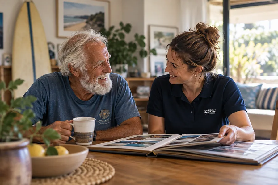 Older man and East Coast Care Connect support worker looking through a photo album together at home.