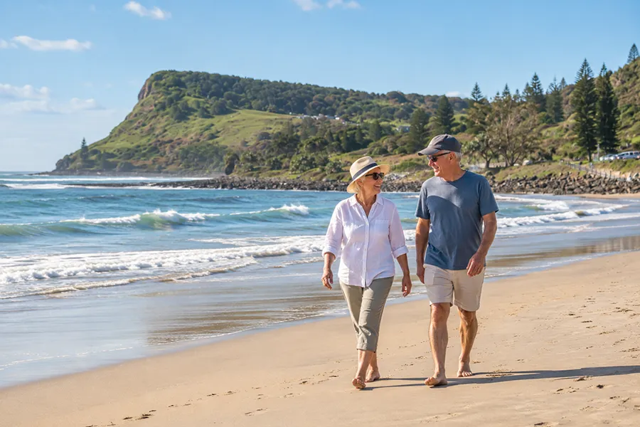 Older couple walking along Lennox Head beach with the headland in the background